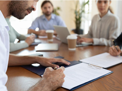 Man signing a document at a table with colleagues