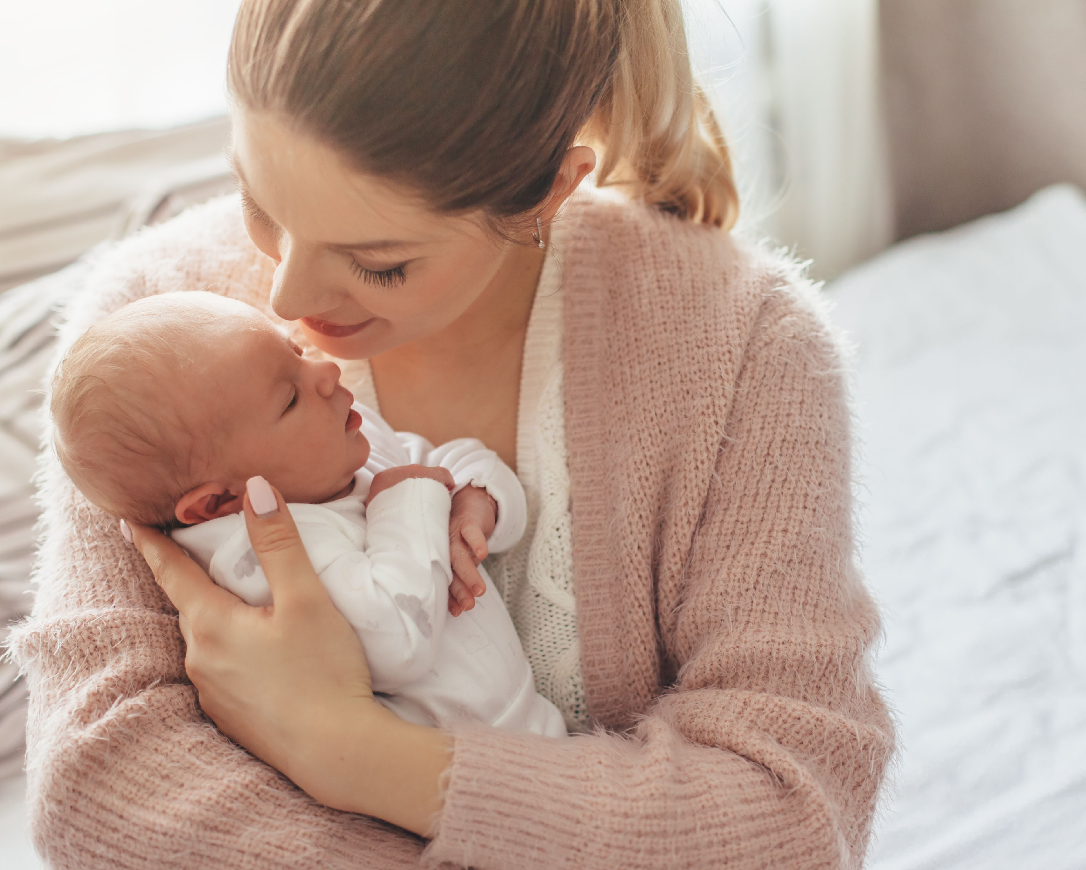 Home portrait of a newborn baby with mother on the bed. Mom holding and kissing her child.