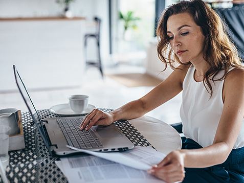 Woman using laptop while sitting at table. Young businesswoman sitting in kitchen and working on laptop