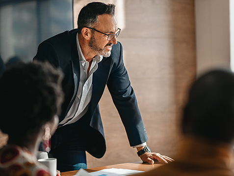 close up of businessman standing over boardroom table in front of South African coworkers during a diverse corporate meeting