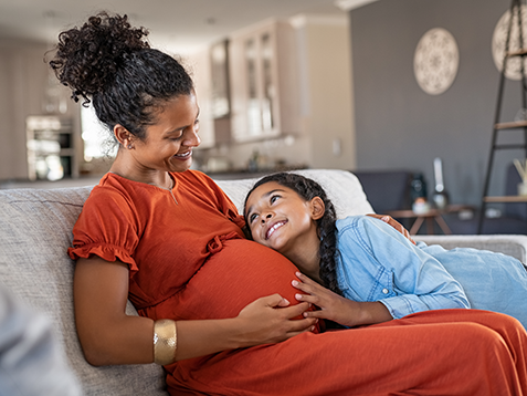 Pregnant mother smiling down at her daughter while sitting on a couch.