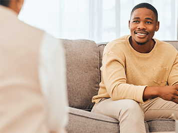 Man sitting on a couch while smiling and talking to someone