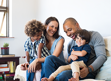 Two parents smiling while holding their two kids and sitting on a couch