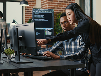 Woman standing next to a male coworker at his desk pointing at a computer screen.