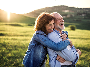 Side view of senior couple hugging outside in spring nature at sunset.