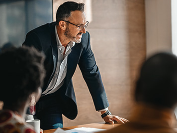 close up of businessman standing over boardroom table in front of South African coworkers during a diverse corporate meeting