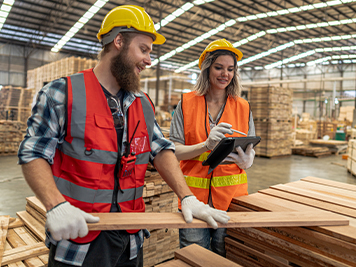 Team workers carpenter wearing safety uniform and hard hat working and checking the quality of wooden products at workshop manufacturing. man and woman workers wood in dark warehouse industry.